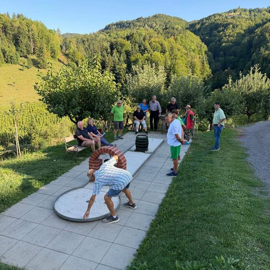 Eine Gruppe von Menschen spielt Minigolf an einem sonnigen Tag in einer malerischen Außenumgebung mit üppiger Vegetation und Bergen im Hintergrund.