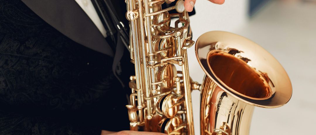 Ein Musiker spielt ein goldenes Saxophon. Das Instrument wird mit beiden Händen gehalten, und die Finger des Musikers sind auf den Tasten positioniert.