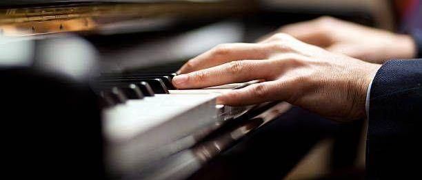 Ein Mann spielt Klavier und benutzt beide Hände. Das Klavier hat eine schwarze und weiße Tastatur. Der Mann trägt einen Anzug.
