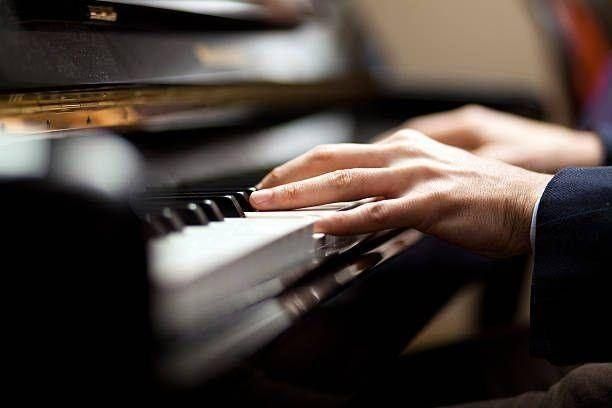 Eine Person in einem Anzug spielt mit beiden Händen Klavier. Das Klavier hat schwarze und weiße Tasten.