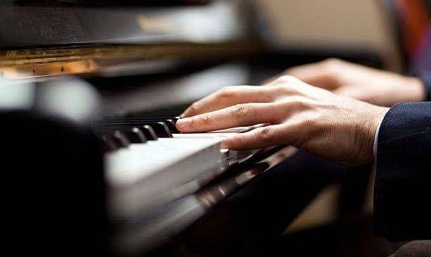 Eine Person in einem Anzug spielt mit beiden Händen Klavier. Das Klavier hat schwarze und weiße Tasten.