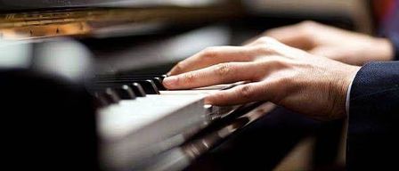 Eine Person spielt Klavier mit Fingern, die die Tasten drücken. Das Klavier ist schwarz und weiß mit einem unscharfen Hintergrund.