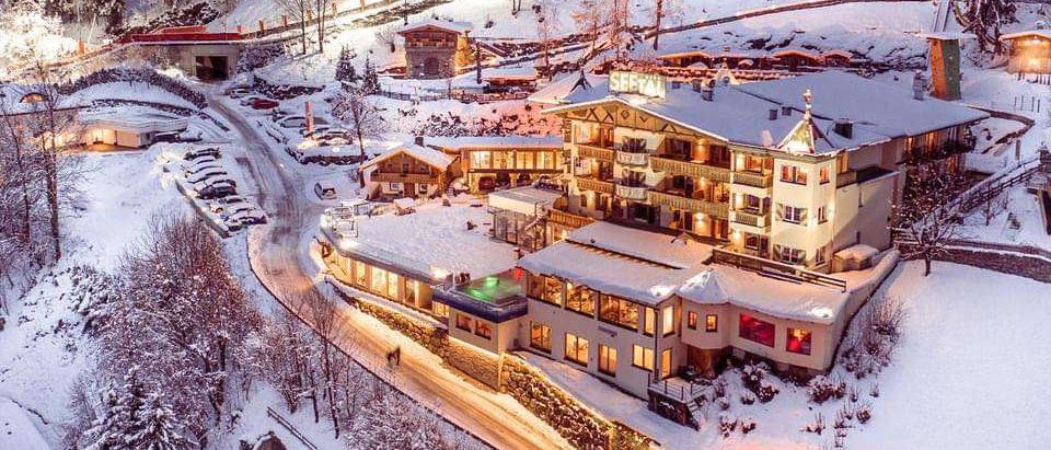 Ein Winter-Luftbild eines Skigebiets mit einem schneebedeckten Hotel und einer Skiabfahrt. Bäume umgeben das Gebiet.