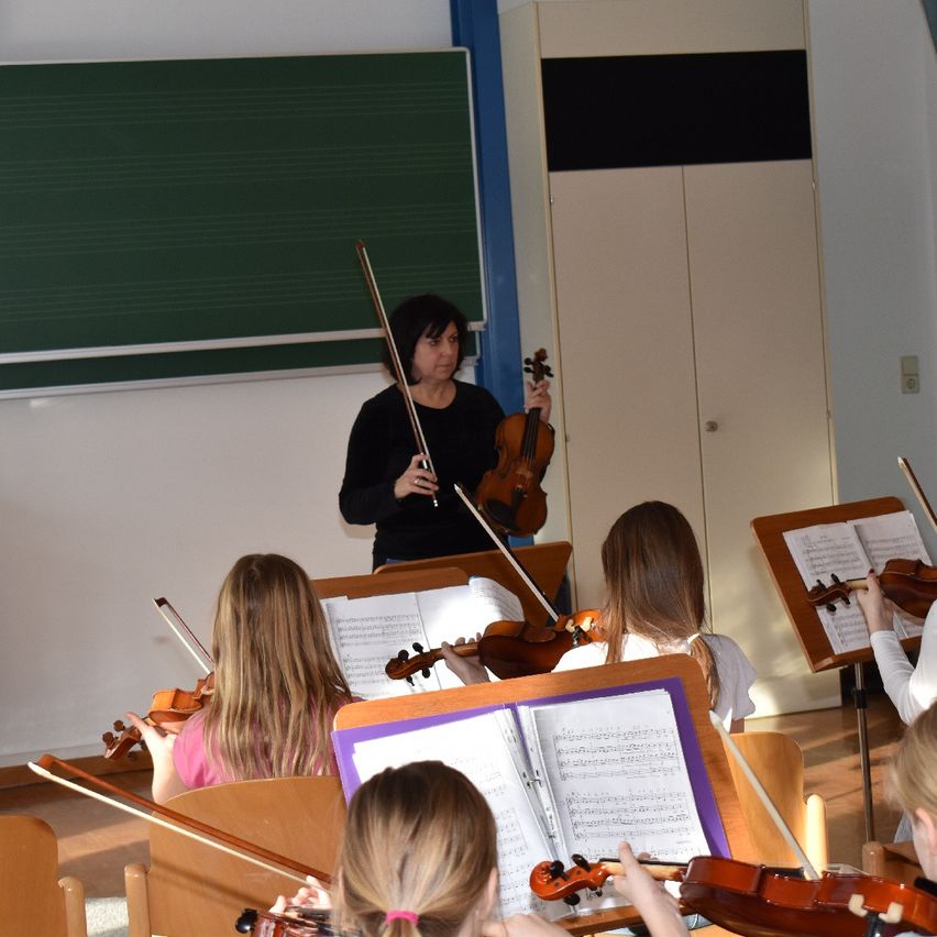 Eine Frau unterrichtet eine Gruppe junger Mädchen im Geigenspiel in einem Klassenzimmer.