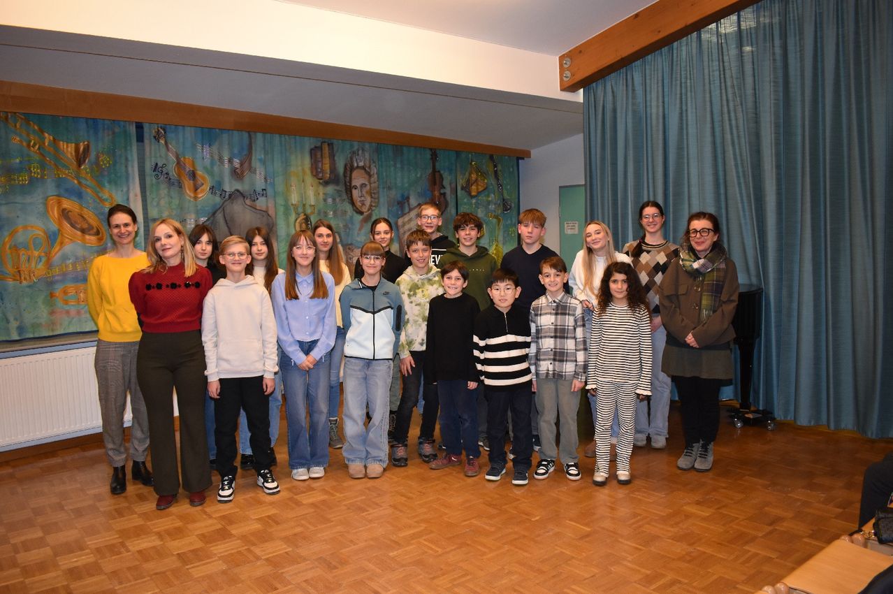 Eine Gruppe von Schülern und Lehrern posiert für ein Foto in einem Raum mit einem musikthematischen Hintergrund.