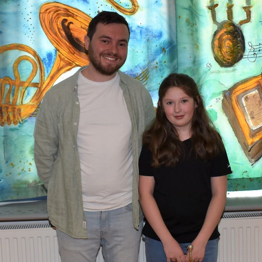 A man and a young girl are standing next to each other in front of a colorful painting. They are both smiling.