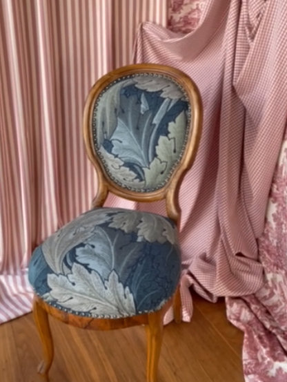 Ein Holzstuhl mit floralem Bezug steht vor einem rosa Vorhang mit Blumenmuster.