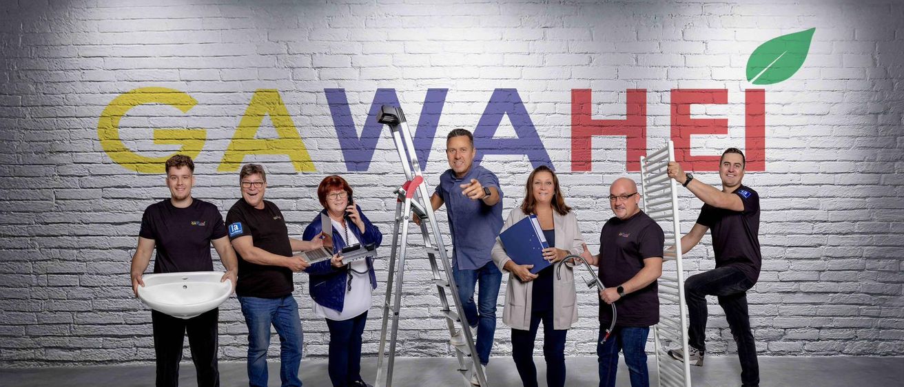 Eine Gruppe von Menschen steht vor einer Backsteinwand mit dem Wort "AWAHE". Ein Mann steht auf einer Leiter und hält ein Gerät. Die anderen haben verschiedene Werkzeuge und Dokumente.