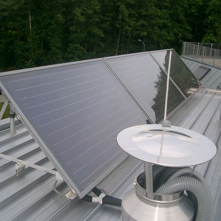 Ein Solarpanel ist auf dem Dach montiert, mit einer silberfarbenen Struktur, möglicherweise ein Solarwarmwasserbereiter, der daran befestigt ist.