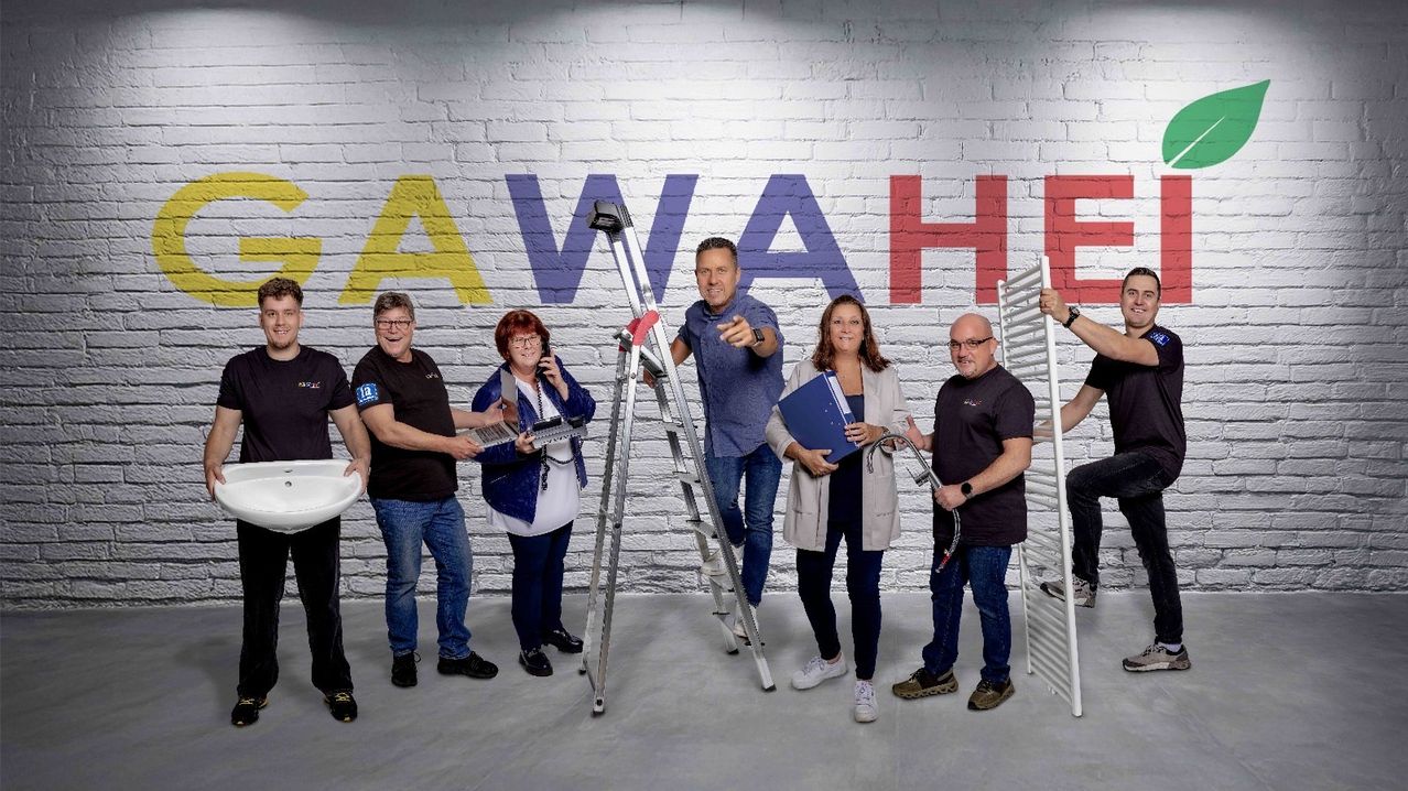Eine Gruppe von Menschen posiert vor einer weißen Ziegelwand mit dem Wort 'AWAVE' in bunten Buchstaben und hält verschiedene Werkzeuge und Dokumente in den Händen.