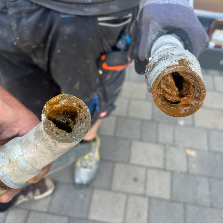 A person holding two dirty pipes with brown residue. One is cut open and the other has a hole.
