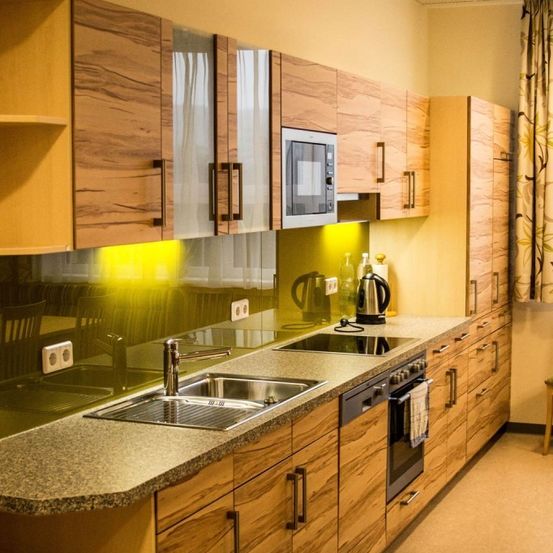 Moderne Küche mit Holzschränken, Granitarbeitsplatten, Edelstahlgeräten und einem Fenster mit Vorhang.