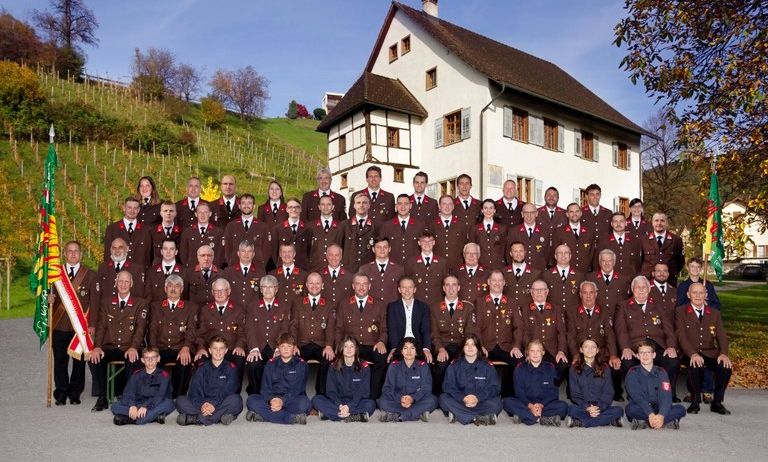 Eine große Gruppe von Menschen in Uniform posiert für ein Foto vor einem Haus mit braunem Dach.