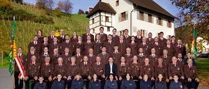 Eine große Gruppe von Menschen in Uniform posiert für ein Foto vor einem Haus mit braunem Dach.