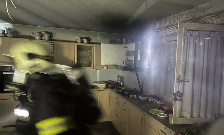 Ein Feuerwehrmann ist in einer Küche, die zu brennen scheint. Die Küche ist schwach beleuchtet, und Rauch steigt aus dem Bereich auf.