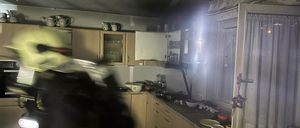 Ein Feuerwehrmann ist in einer Küche, die zu brennen scheint. Die Küche ist schwach beleuchtet, und Rauch steigt aus dem Bereich auf.