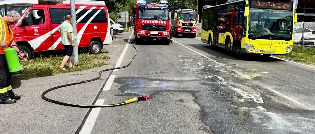 Ein Mann geht neben einem Feuerwehrauto mit einer Schlauchleitung auf der Straße. Andere Rettungsfahrzeuge sind in der Nähe geparkt.