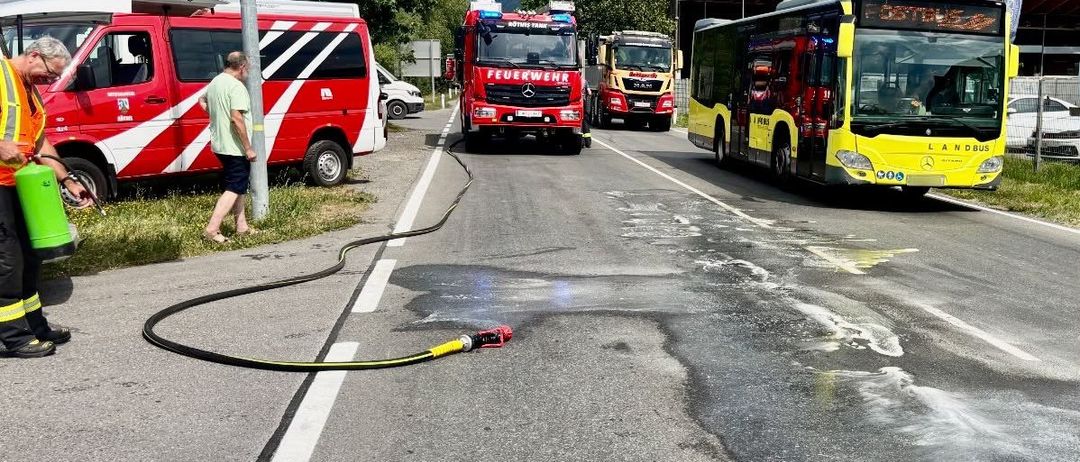 Ein Mann geht neben einem Feuerwehrauto mit einer Schlauchleitung auf der Straße. Andere Rettungsfahrzeuge sind in der Nähe geparkt.