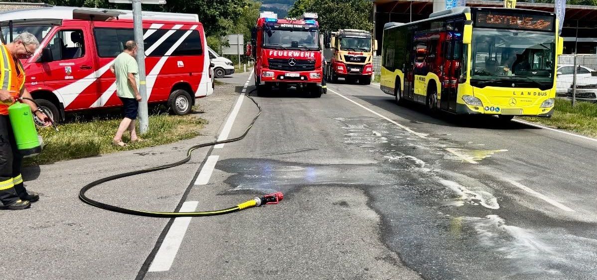 Ein Mann geht neben einem Feuerwehrauto mit einer Schlauchleitung auf der Straße. Andere Rettungsfahrzeuge sind in der Nähe geparkt.