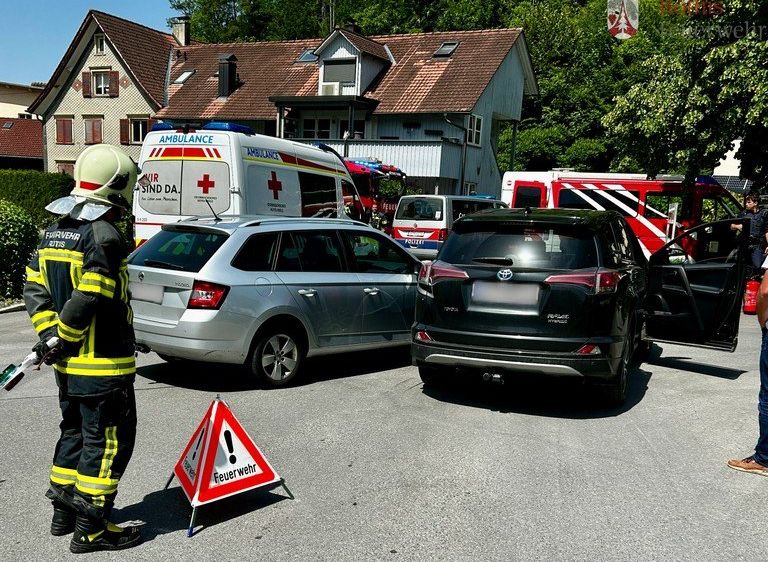 Ein Feuerwehrmann steht neben einem Feuerwehrwagen und einem Krankenwagen am Straßenrand mit zwei beschädigten Autos.