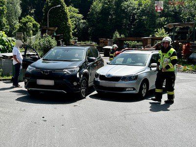 Zwei Autos sind am Straßenrand geparkt, wobei Rettungskräfte sie betreuen. Ein Mann in einem weißen Shirt steht in der Nähe des schwarzen Autos.