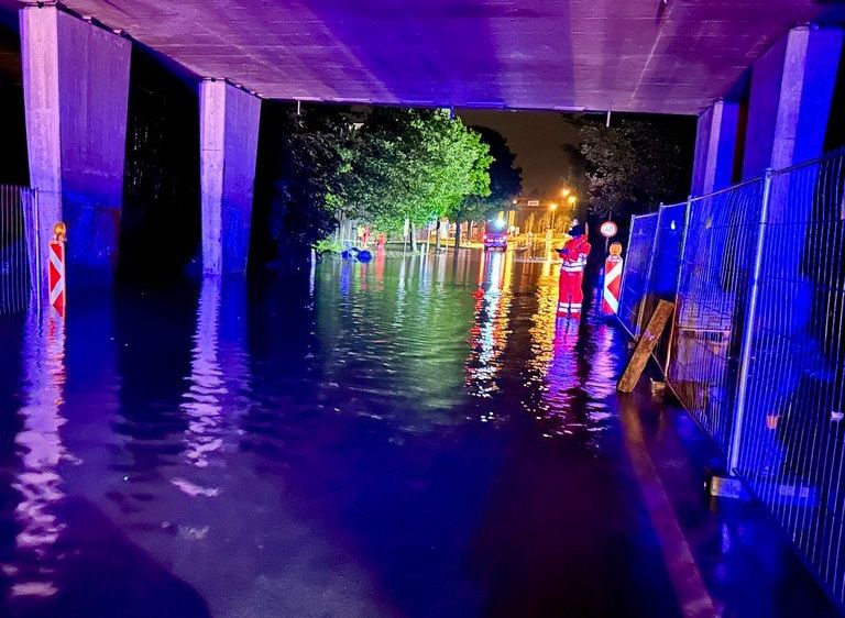 Eine überflutete Straße bei Nacht mit Notfallpersonal in roten Uniformen in der Nähe einer Brücke.