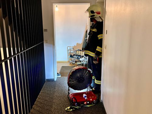 Ein Feuerwehrmann steht in einem Flur mit einem großen roten Ventilator und einem Helm auf.