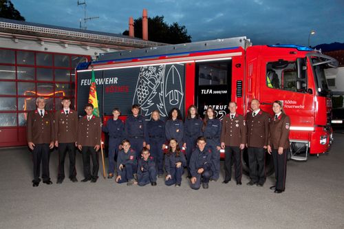 Eine Gruppe Feuerwehrleute in Uniform vor einem Feuerwehrauto mit einer Flagge.