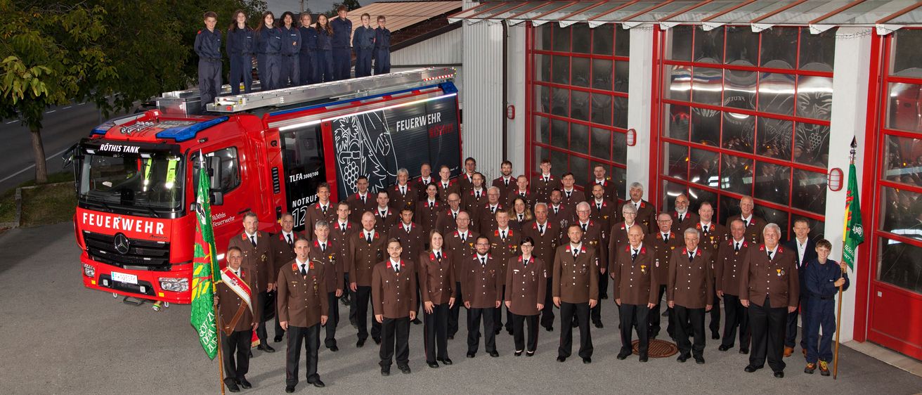 Eine Gruppe von Feuerwehrleuten in Uniform steht vor einem Feuerwehrauto, einige stehen darauf.