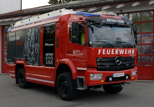 Ein roter Feuerwehrwagen mit der Aufschrift 'FEUERWEHR' auf der Vorderseite und der Nummer 122 an der Seite. Der Wagen hat ein Logo und den Namen 'Rothis' auf der vorderen Tür.