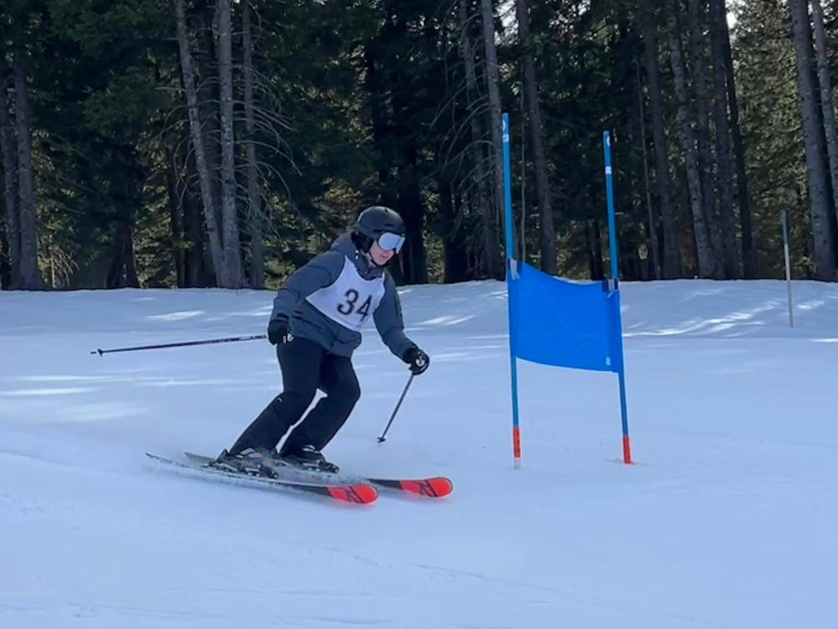 Ein Skifahrer mit der Nummer 34 fährt einen verschneiten Hang hinunter und passiert ein blaues Hindernis.