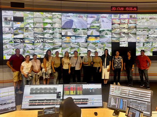 Eine Gruppe von Frauen steht vor einem großen Monitor mit mehreren Verkehrskamerabildern und einer digitalen Uhr.
