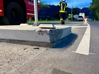 Ein Feuerwehrmann geht in der Nähe einer beschädigten Betonbordsteins. Ein Krankenwagen und ein Feuerwehrauto sind geparkt. Ein Fahrzeug ist im Hintergrund zu sehen.