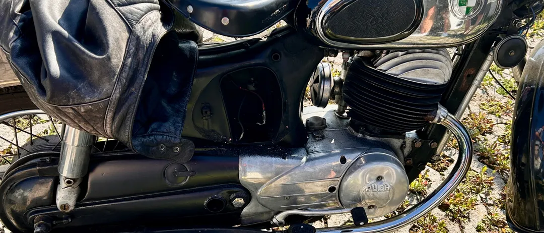 Ein schwarzes Vintage-Motorrad mit Chrom-Akzenten und einem Ledersitz steht auf einem Kopfsteinpflasterweg.
