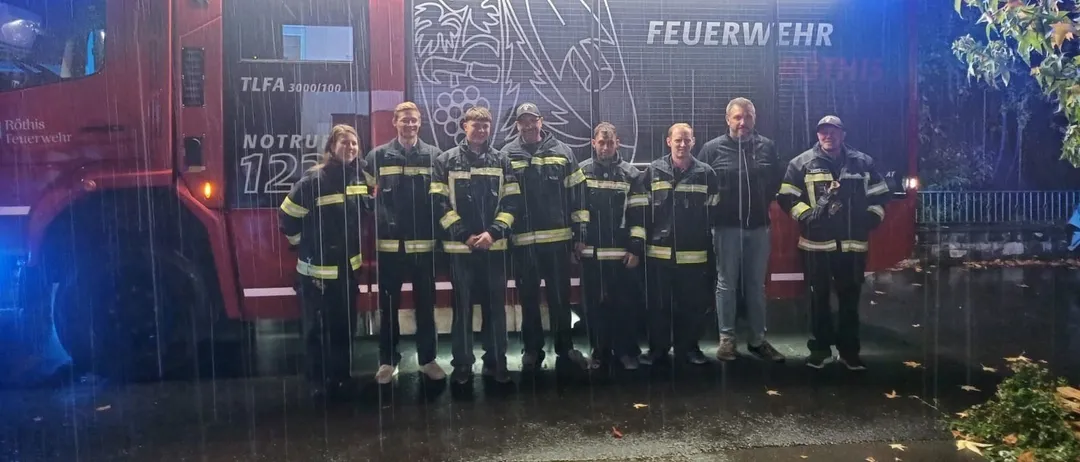 Eine Gruppe von Feuerwehrleuten steht vor einem roten Feuerwehrauto im Regen.