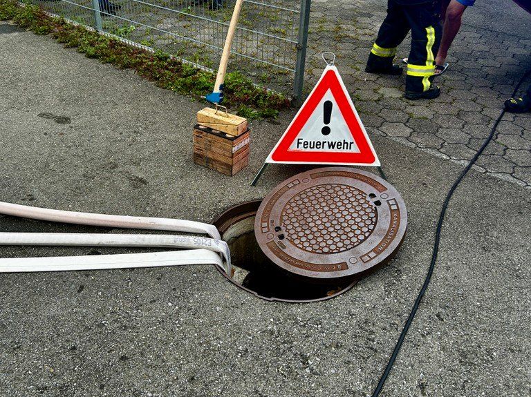 Ein Feuerwehrmann benutzt ein Werkzeug zur Inspektion eines Kanaldeckel, mit einem Warnschild an der Seite.