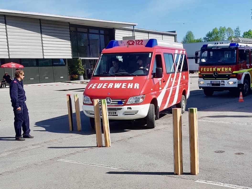 Ein roter Feuerwehrwagen ist vor einem Gebäude geparkt, in dem zwei Personen sitzen, vor einem Gebäude.