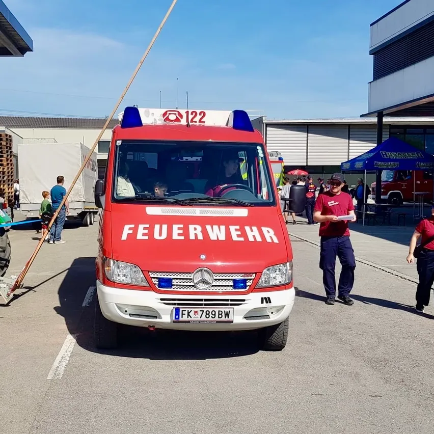 Ein roter Feuerwehrwagen mit der Aufschrift "Feuerwehr" mit einem blauen Licht oben und einer Person im Inneren. Der Fahrer fährt mit offenem Motorhauben.