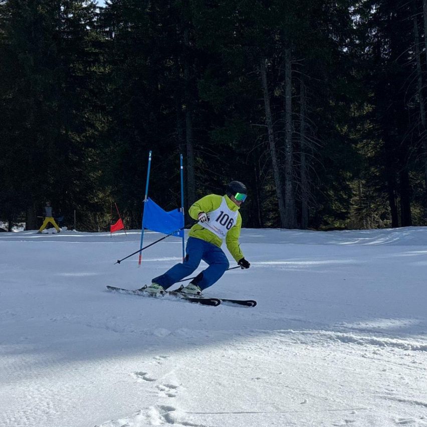 Ein Skifahrer in einem gelben Jackett mit der Nummer 106 navigiert durch einen verschneiten Parcours mit blauen Flaggen.