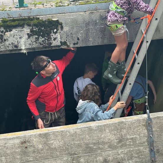 Eine Gruppe von Menschen ist an einer Baustelle tätig. Eine Person klettert eine Leiter hinauf, während andere helfen.