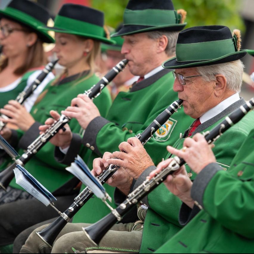 Eine Gruppe von Musikern in grünen Uniformen und Mützen spielt ihre Klarinetten bei einem Konzert. Die Klarinetten haben blaue Mundstücke und liegen auf ihren Knien.