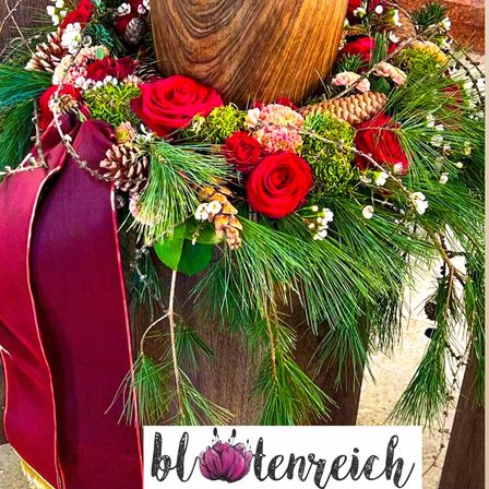Ein hölzerner Pfosten ist mit einem Kranz aus roten Rosen, Tannenzapfen und Grün geschmückt. Der Kranz besteht aus verschiedenen saisonalen Pflanzen. Der Pfosten ist braun und hat ein Wasserzeichen mit dem Text 'blottenreich'.
