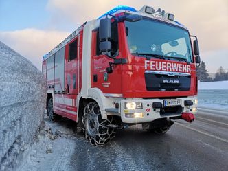 Ein roter und weißer Feuerwehrwagen mit dem Wort 'Feuerwehr' auf der Front, auf einer verschneiten Straße geparkt.