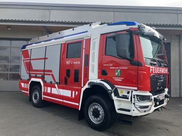 Ein roter und weißer Feuerwehrwagen mit der Aufschrift 'HLF 2 4000/100' steht vor einem Gebäude.