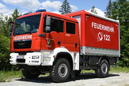 Ein roter Feuerwehrwagen mit der Nummer 12 auf der Seite ist auf einem Schotterweg geparkt. Er hat einen weißen Stoßfänger und eine blaue Lampe oben.