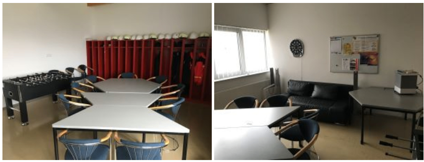 Ein Raum mit weißen Wänden, Tischen und Stühlen. Links befindet sich ein roter Schrank mit Helmen oben. Rechts steht eine Couch und eine Pinnwand.