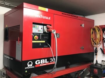 Ein großer roter Generator mit der Aufschrift GBL 30 Power Engineering. Er hat einen roten Netzschalter und ein rotes Stromkabel angeschlossen.