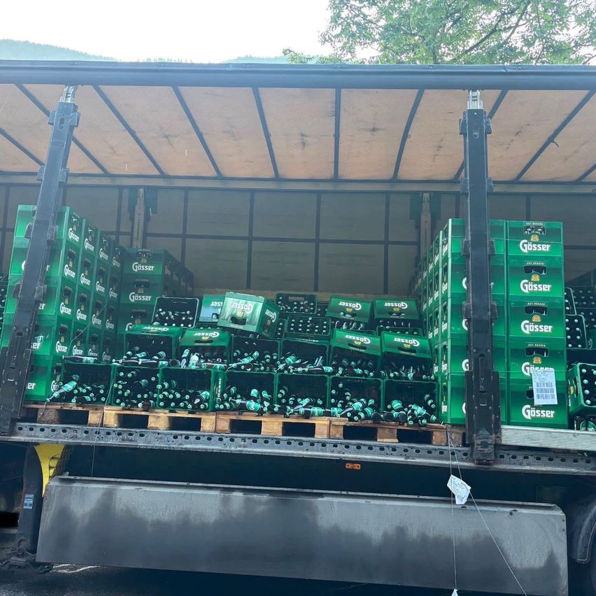 Ein Lkw, beladen mit grünen Kisten Güsser-Bier, auf Holzpaletten gestapelt. Die Kisten sind dicht gepackt, und das Dach des Lkw ist mit einer Plane abgedeckt.