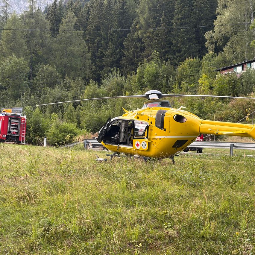 Ein gelber Hubschrauber mit einem roten Kreuz auf der Seite ist auf einem Grasfeld geparkt. Ein roter Feuerwehrwagen ist dahinter geparkt. Der Hubschrauber scheint auf dem Gras gelandet zu sein.