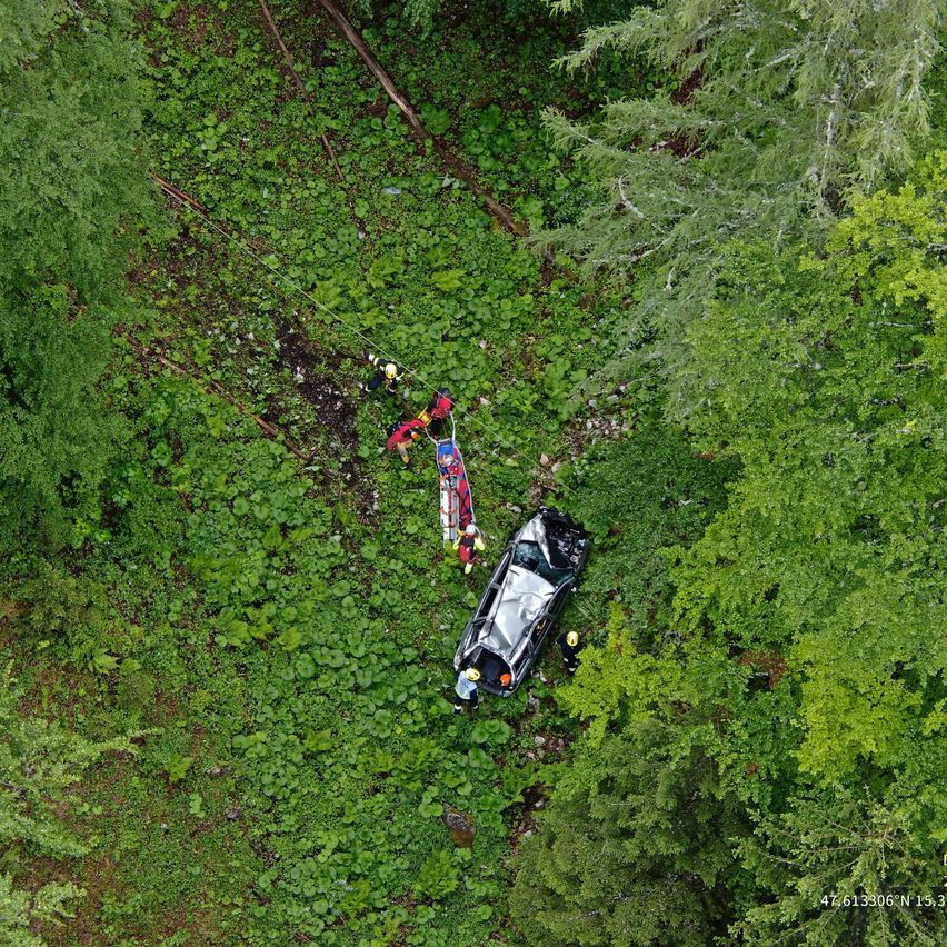 Ein Autounfall ereignete sich im Wald, bei dem Rettungskräfte das Fahrzeug aus dem Wald ziehen. Das Auto liegt auf der Seite.